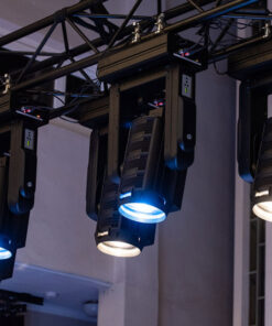 Le luci da palcoscenico della collezione TV Serie Hyperion per Teatri e Studi sono appese a un'attrezzatura metallica, che proietta un chiarore blu. L'attrezzatura è situata vicino a una parete bianca, con parte del soffitto in vista.