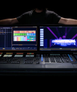 Una persona aziona la console di controllo luci Eos Apex 20, dotata di due grandi schermi che mostrano le impostazioni colore e un layout del palco con effetti di luce. La console è dotata di vari pulsanti e cursori, tutti impostati su uno sfondo scuro.