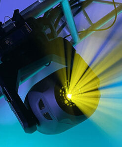 Un riflettore da palco Lonestar è montato su un'attrezzatura metallica, proiettando fasci di luce giallo brillante su uno sfondo blu e verde. La luce genera un effetto dinamico e vibrante, evocando l'atmosfera di uno spettacolo o di un evento.